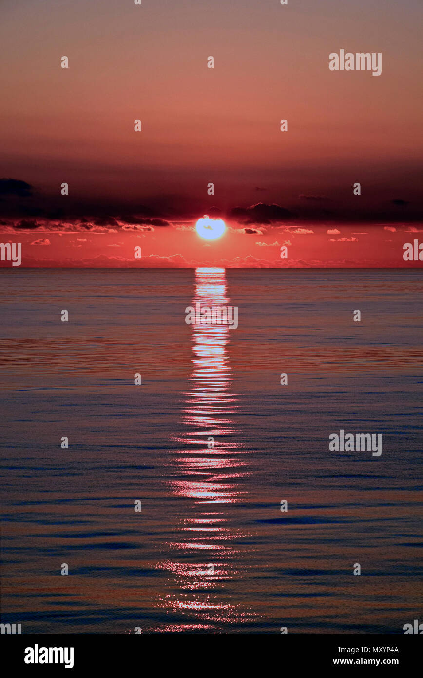 La riflessione di rosso tramonto su un mare liscio Foto Stock