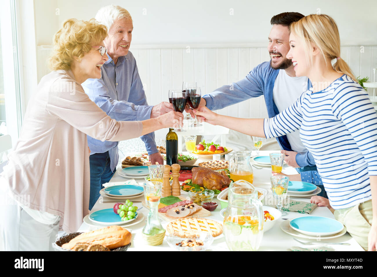 Vista laterale ritratto di felice due famiglia di generazione di gustare la cena insieme tintinnanti bicchieri a mensa conviviale con piatti deliziosi e sorridente durante Foto Stock