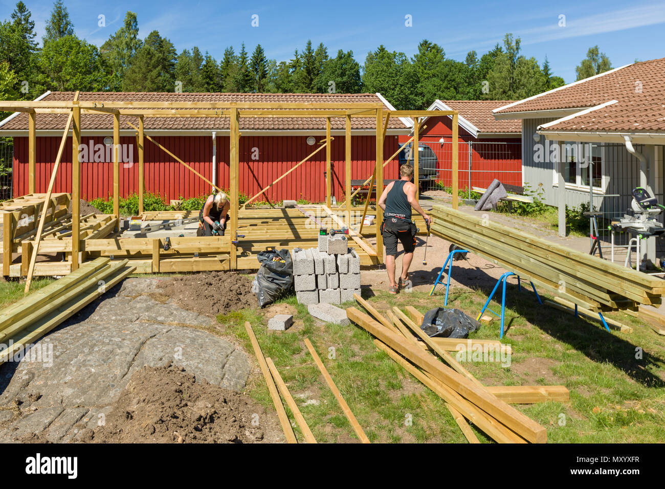 Falegnami per lavorare in esterno a erigere un grande patio con pergola e round firepit Foto Stock