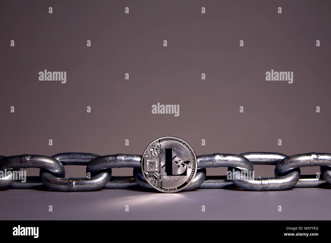 Un LiteCoin siede su una superficie bianca mentre un acciaio pesante catena di metallo si siede dietro. Concetti di catena di blocco di tecnologia e di valuta digitale. Foto Stock