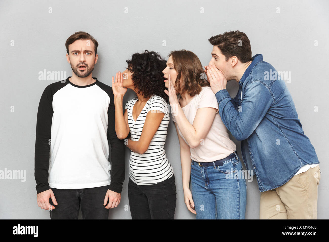 Immagine di un gruppo di amici in piedi isolate su muro grigio Sfondo spettegolare raccontano i segreti di parlare con l'altro. Foto Stock