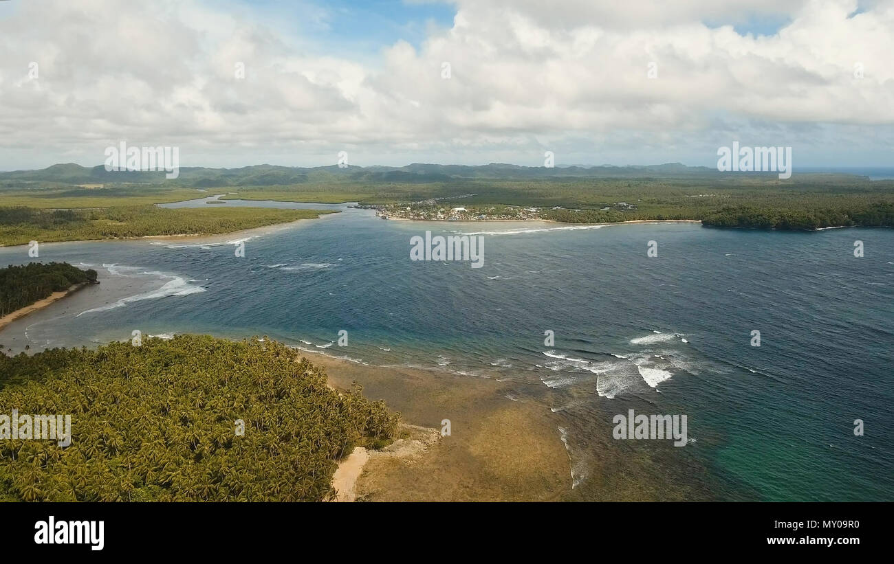 Costa dell'isola tropicale Siargao con le montagne e la foresta pluviale su uno sfondo di oceano con grandi onde. Vista aerea: mare e l'isola tropicale con rocce, la spiaggia e le onde. Seascape: sky, nuvole oceano. Filippine. Concetto di viaggio. Foto Stock
