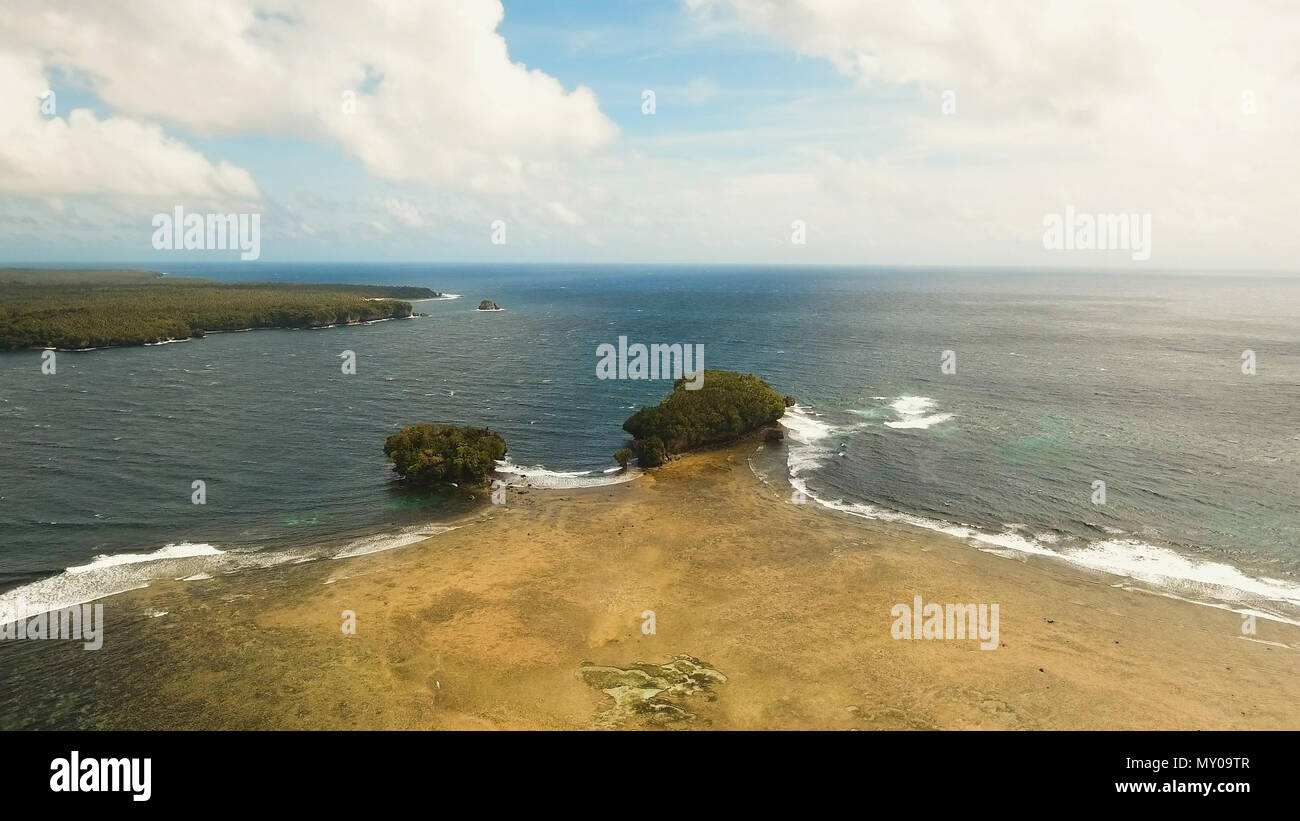 Vista aerea: mare e l'isola tropicale con rocce, la spiaggia e le onde. Costa dell'isola tropicale Siargao con le montagne e la foresta pluviale su uno sfondo di oceano con grandi onde. Seascape: sky, nuvole oceano. Filippine. Concetto di viaggio. Foto Stock