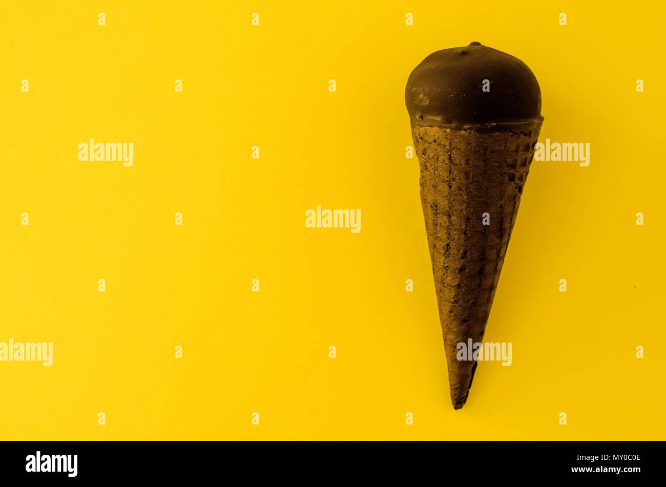 Gelato alla vaniglia con marmellata di mirtilli in un cono di zucchero immersi nel cioccolato su sfondo giallo.color pastello.raffreddare in estate calda.Copia spazio a sinistra Foto Stock