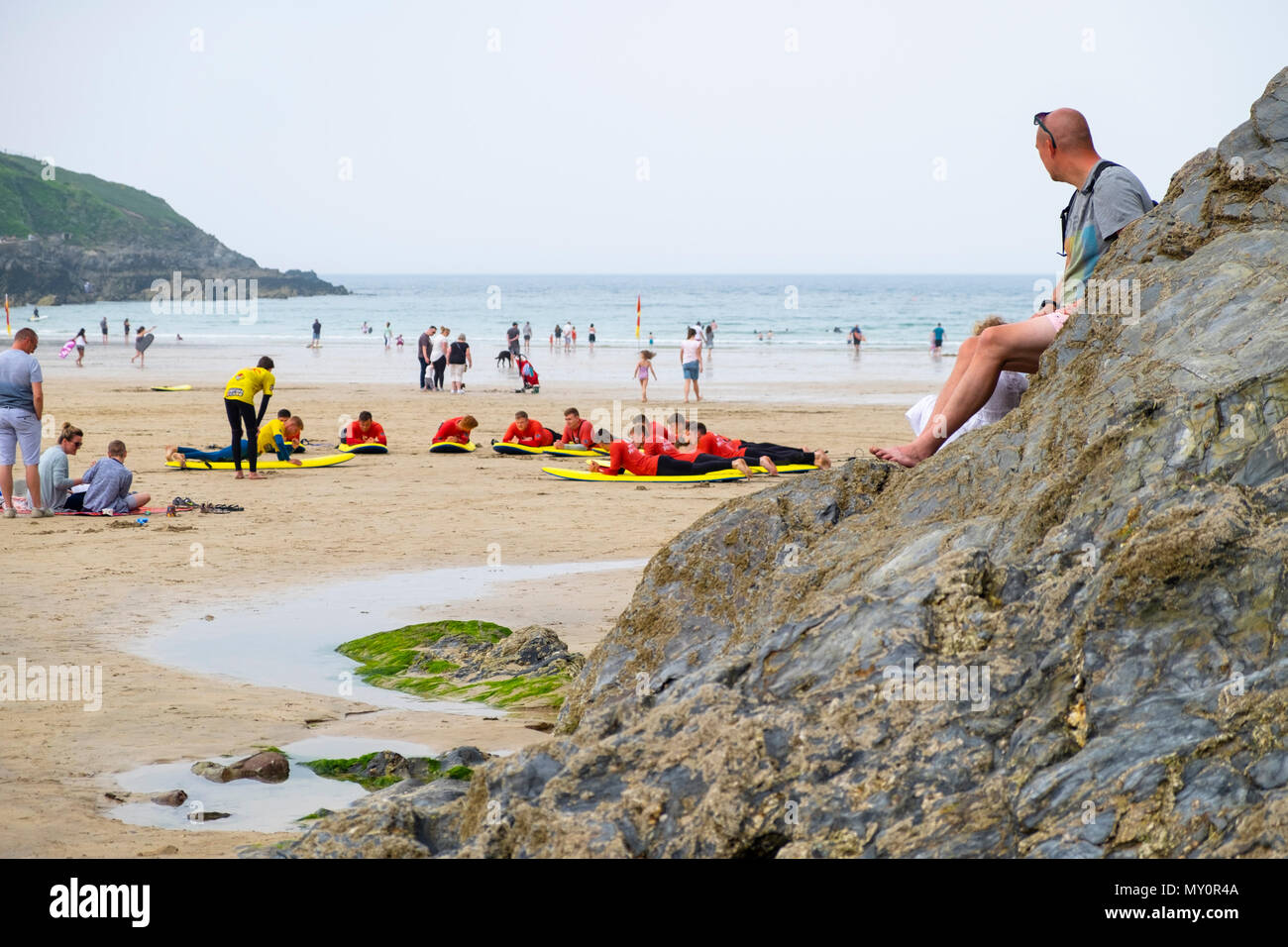 Un uomo guarda su come scuola di surf le lezioni hanno luogo sulla Fistral Beach, Newquay, Regno Unito Foto Stock