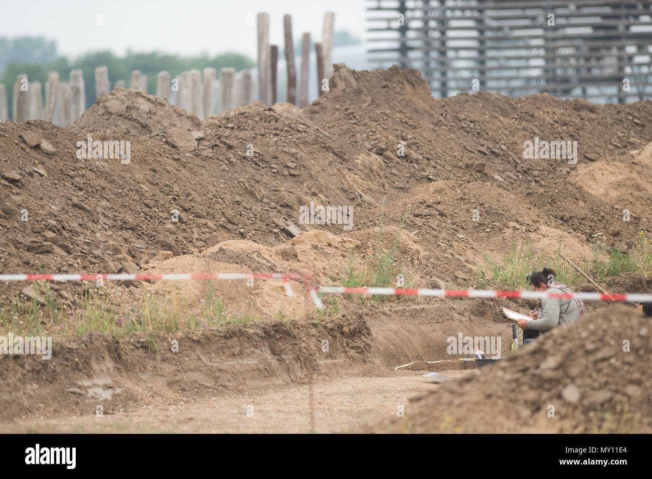 05 giugno 2018, Germania, Poemmelte: un cassetto di scavo lavora in uno strato inferiore ai margini del recinto circolare, dove rimane di un longhouse fascio da una Età del Bronzo Antico insediamento. Il luogo di culto può essere visto in background. La Sassonia-Anhalt Dipartimento del patrimonio e archeologia effettua scavi presso il sito al fine di scoprire se l'Età del Bronzo Antico insediamento e il recinto circolare existet allo stesso tempo. Finora, resti di 13 longhouses sono stati trovati. Foto: Klaus-Dietmar Gabbert/dpa-Zentralbild/ZB Foto Stock