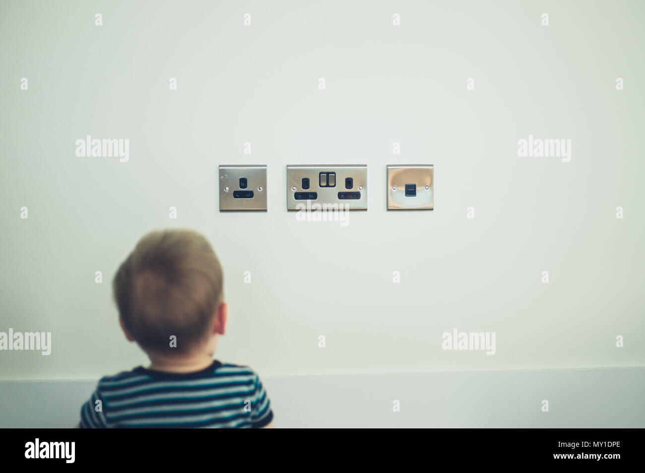 Un piccolo bambino è seduto e guardando prese a spina sulla parete Foto Stock