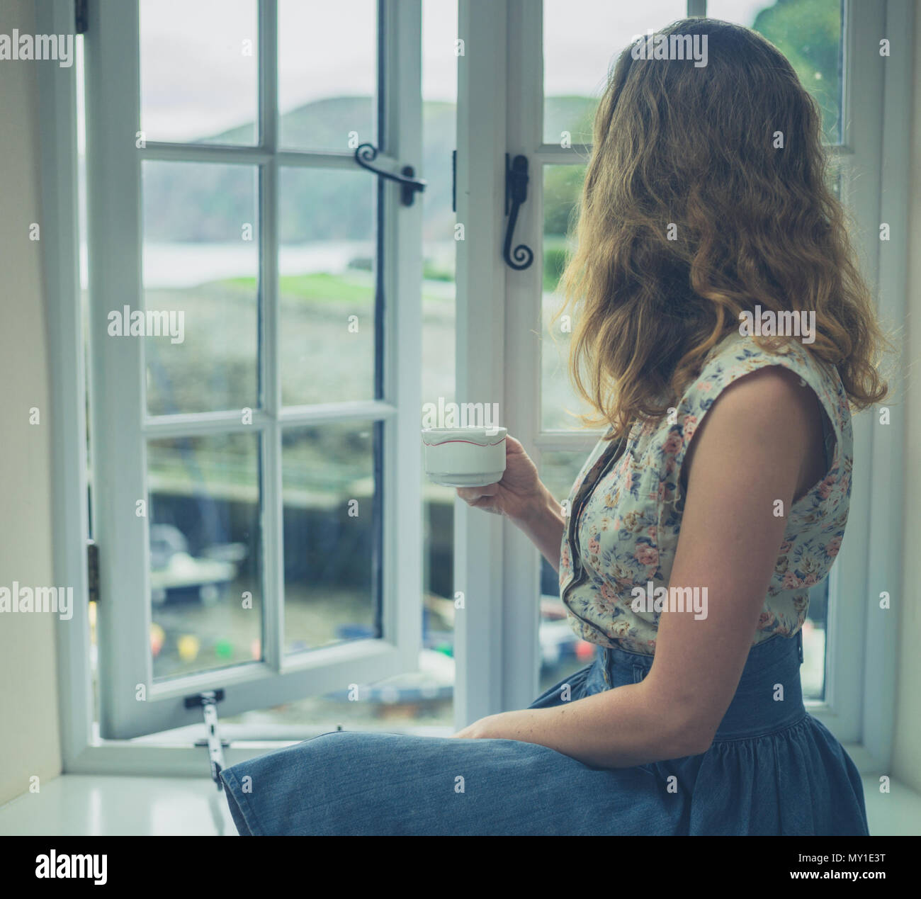 Una giovane donna è drinkng tea dalla finestra di una casa di campagna Foto Stock