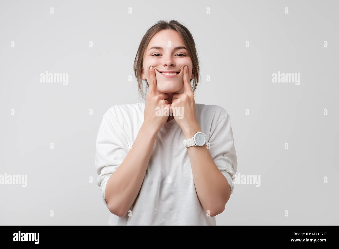 Colpo di caucasici bella ragazza adolescente forzando un sorriso, tenendo le dita in corrispondenza dei bordi delle labbra Foto Stock