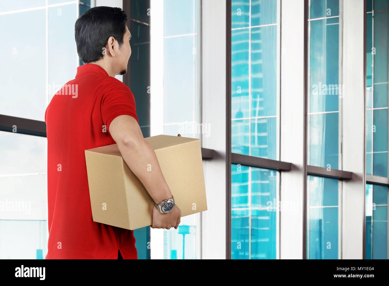 Vista posteriore del maschio asiatici courier tenendo il pacco per l'ufficio Foto Stock