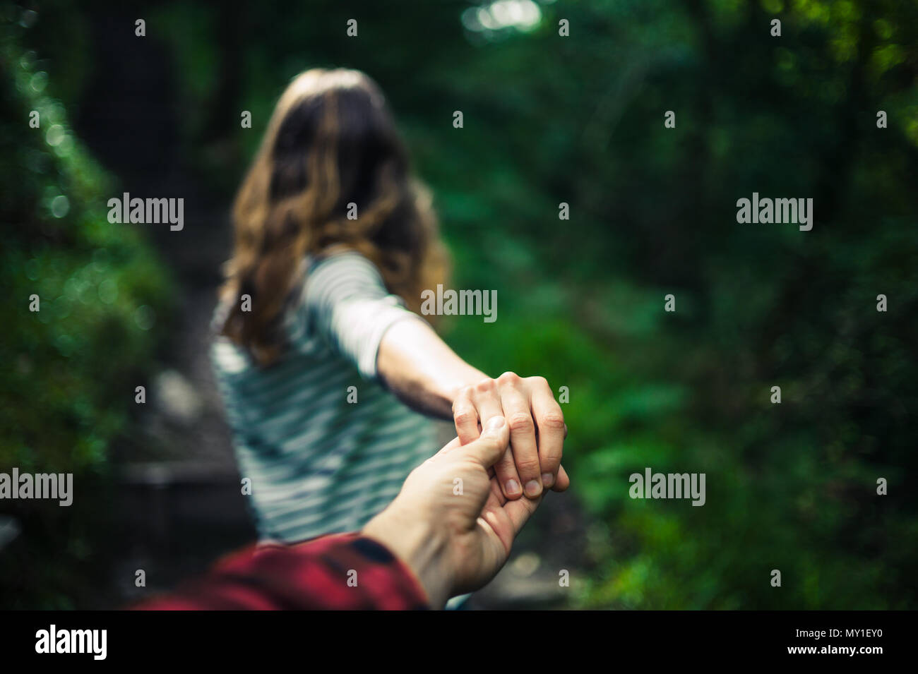 Una giovane donna è guidare il suo fidanzato con la mano in una foresta Foto Stock