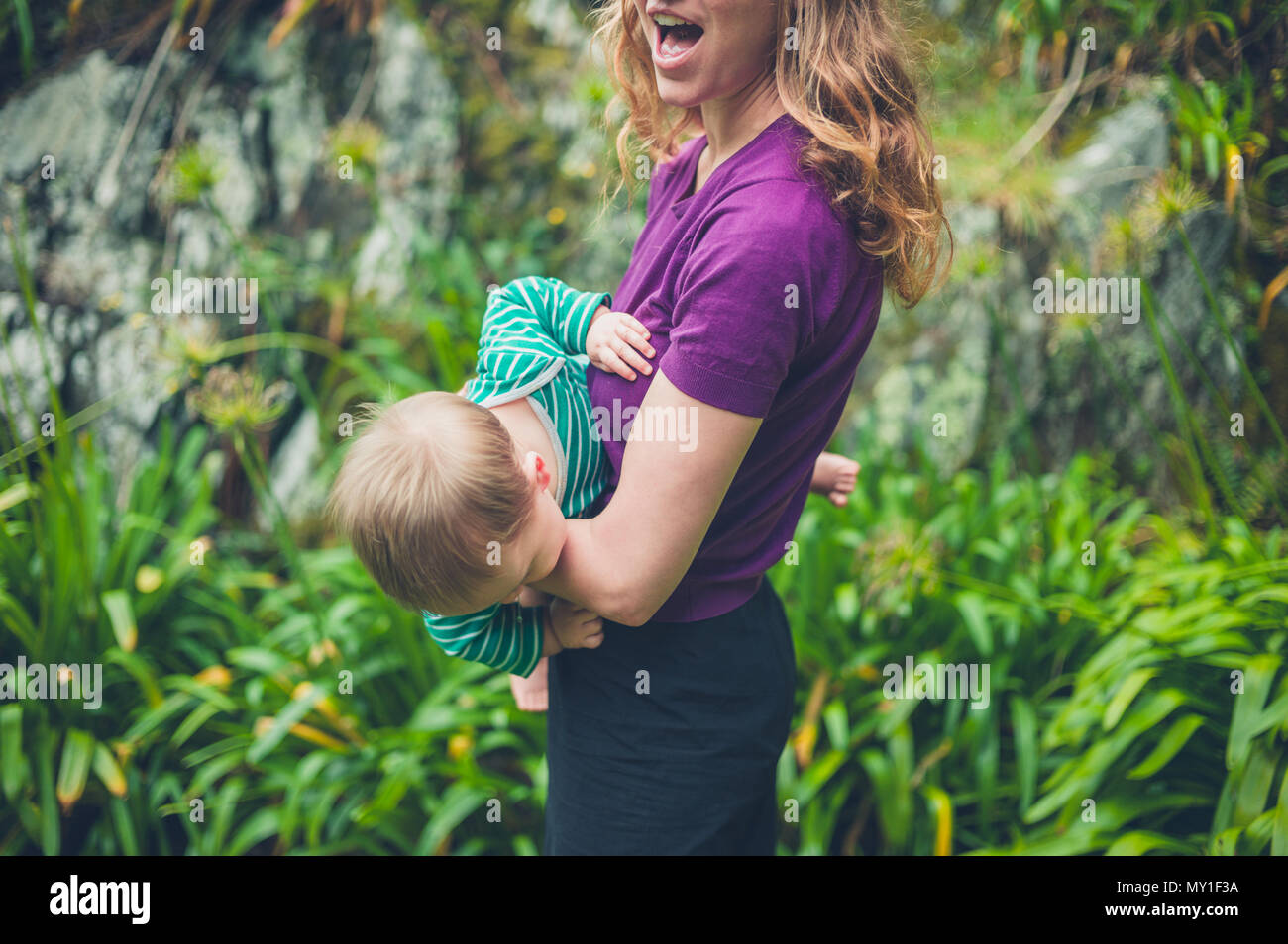 Una giovane madre sta giocando con il suo bambino al di fuori in natura da alcune rocce Foto Stock