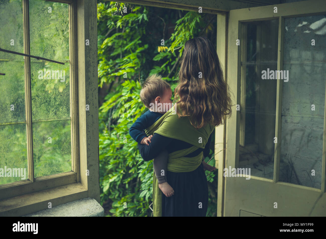 Una madre con il suo bambino in una imbracatura è in piedi nel vano della porta di un conservatorio Foto Stock