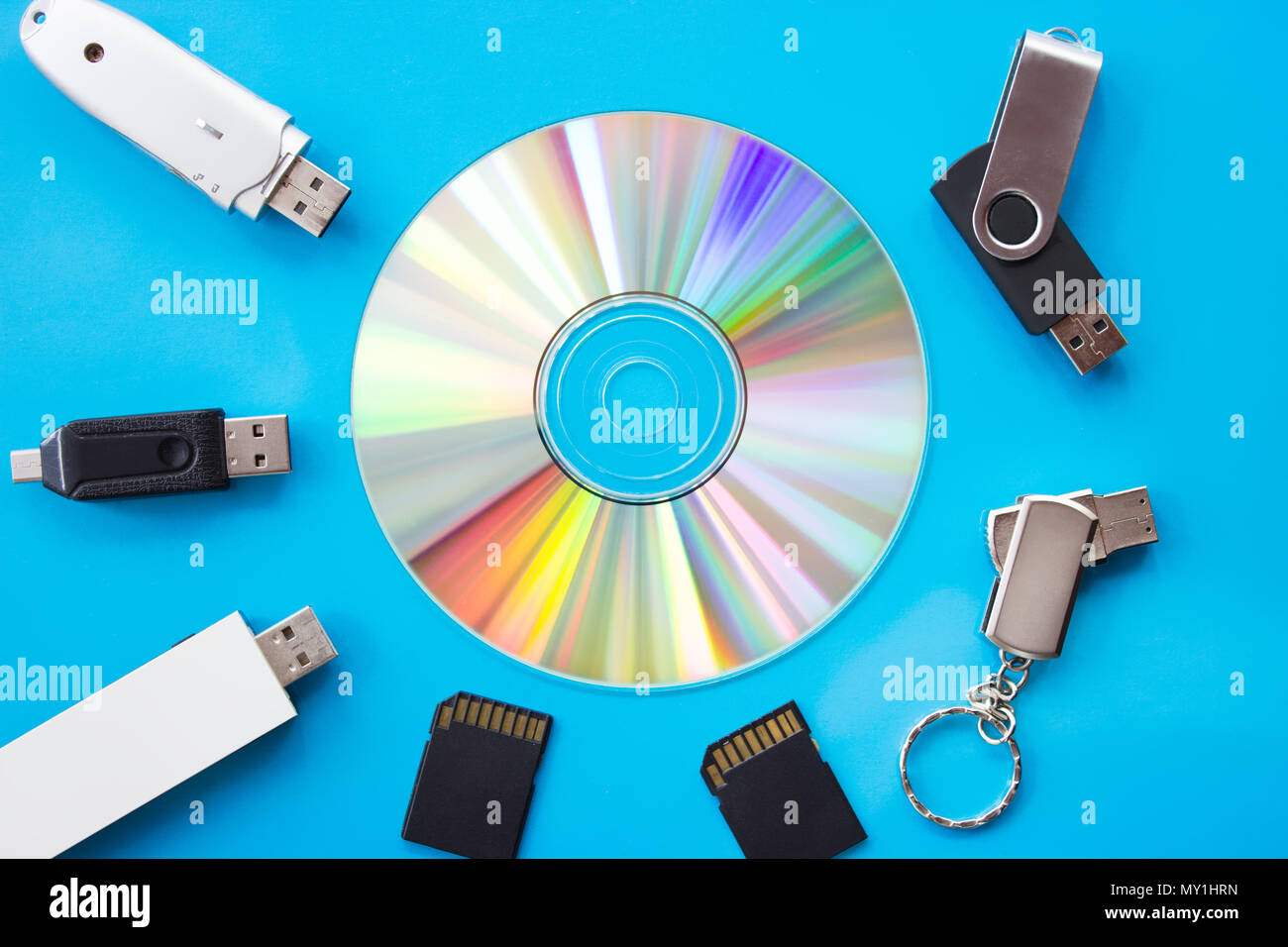 DVD incandescente con arcobaleno di colori su una scheda blu con le unità flash USB e schede - Fotografia flatlay Foto Stock