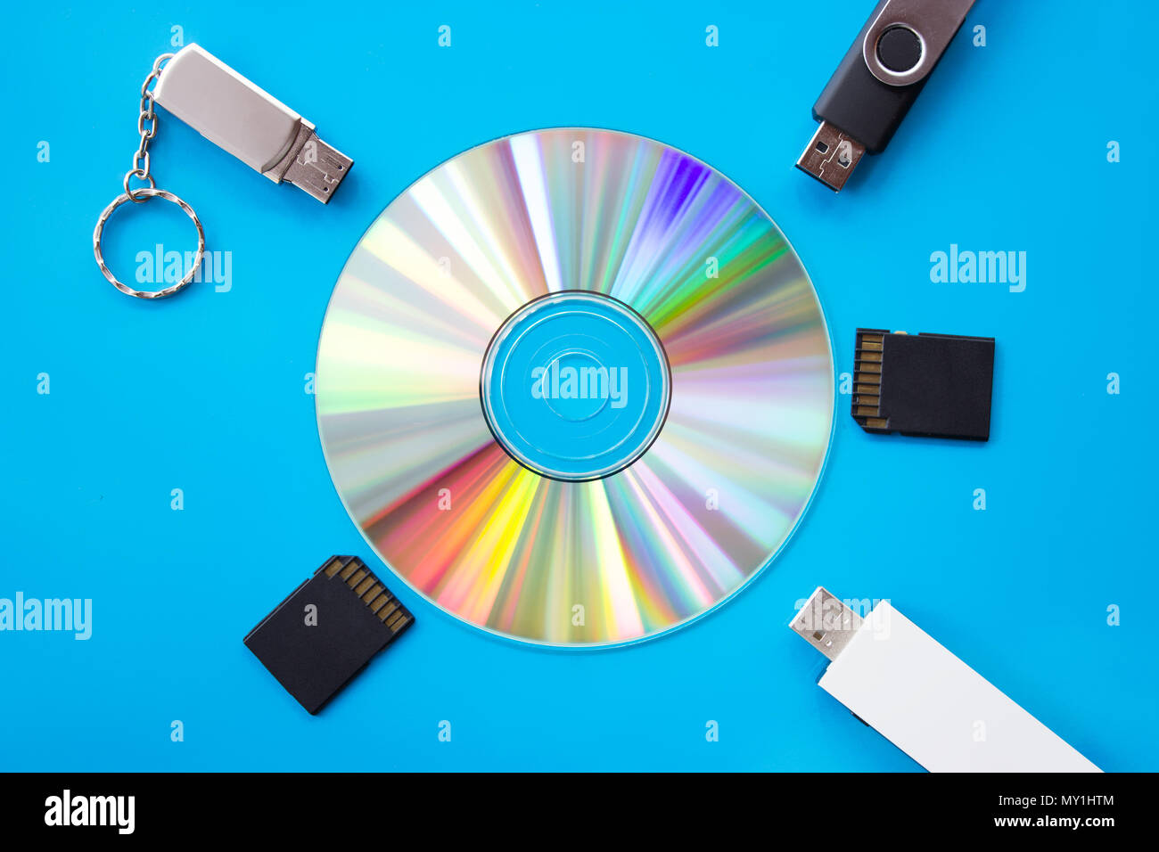 DVD incandescente con arcobaleno di colori su una scheda blu con le unità flash USB e schede - Fotografia flatlay Foto Stock