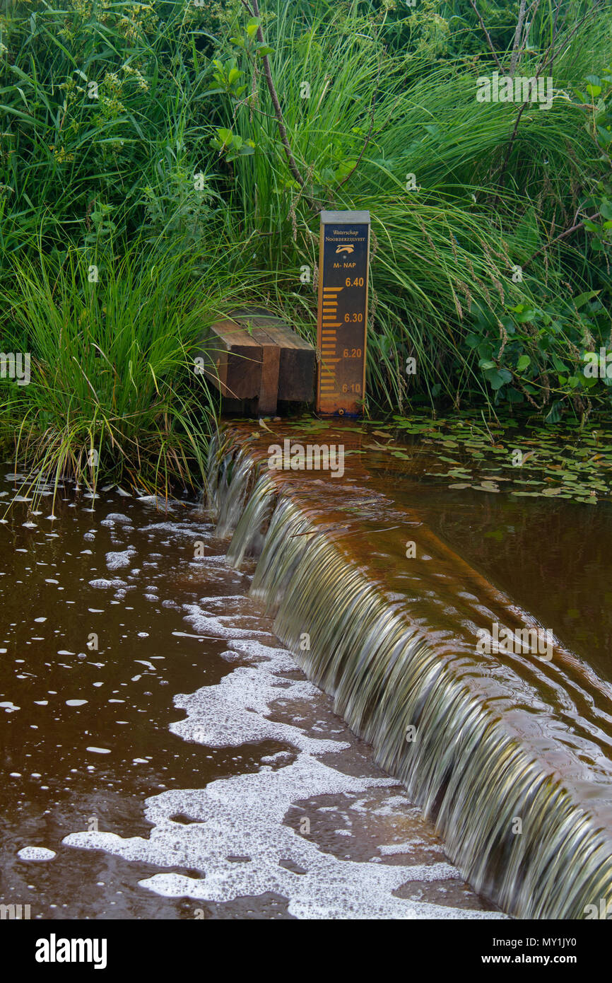 Gestione delle risorse idriche: un piccolo weir e di un misuratore di livello in un fiume olandese Foto Stock