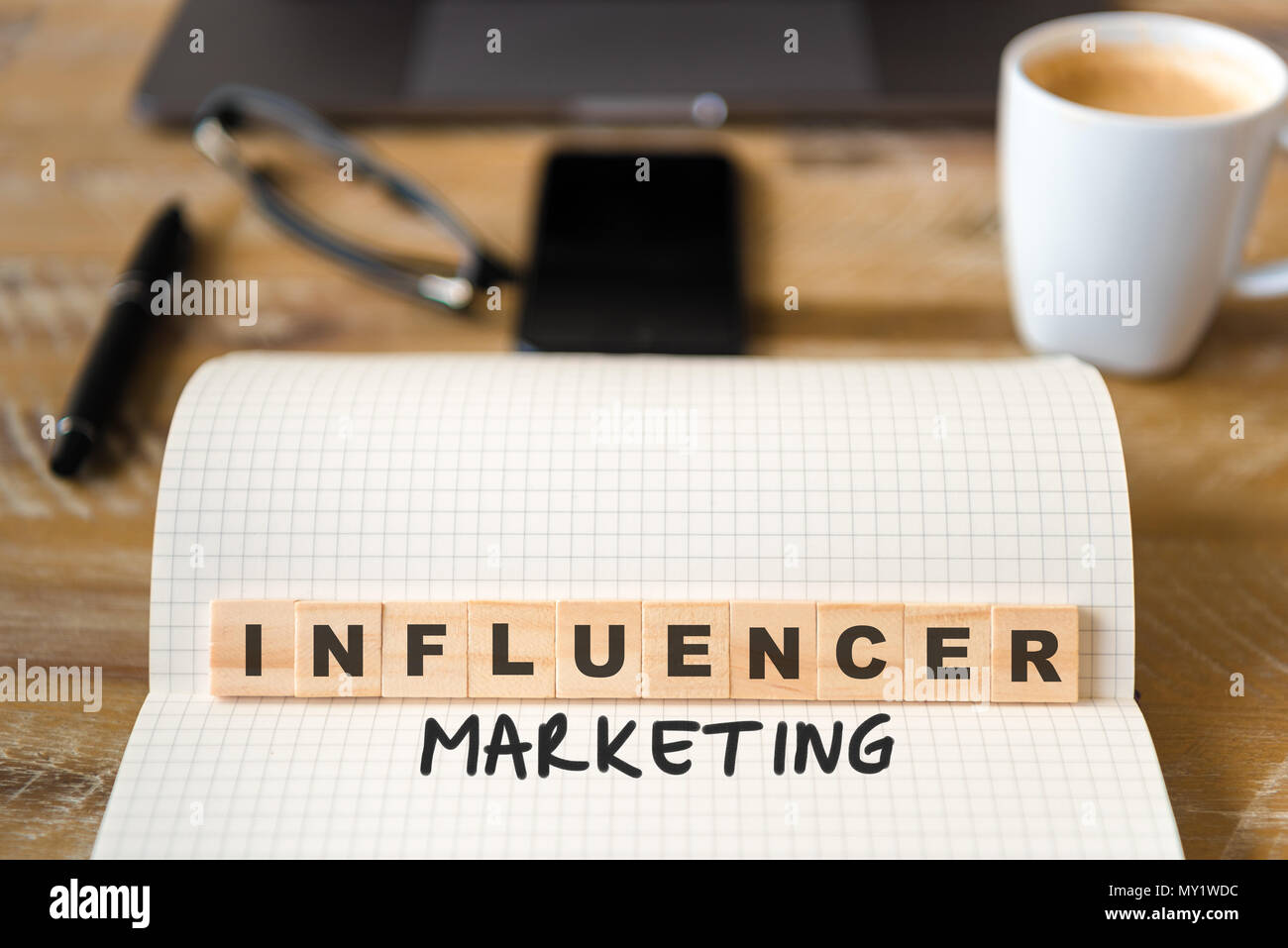 Primo piano su notebook su tavola di legno sfondo, concentrarsi sui blocchi di legno con lettere che Influencer Marketing testo. Foto Stock