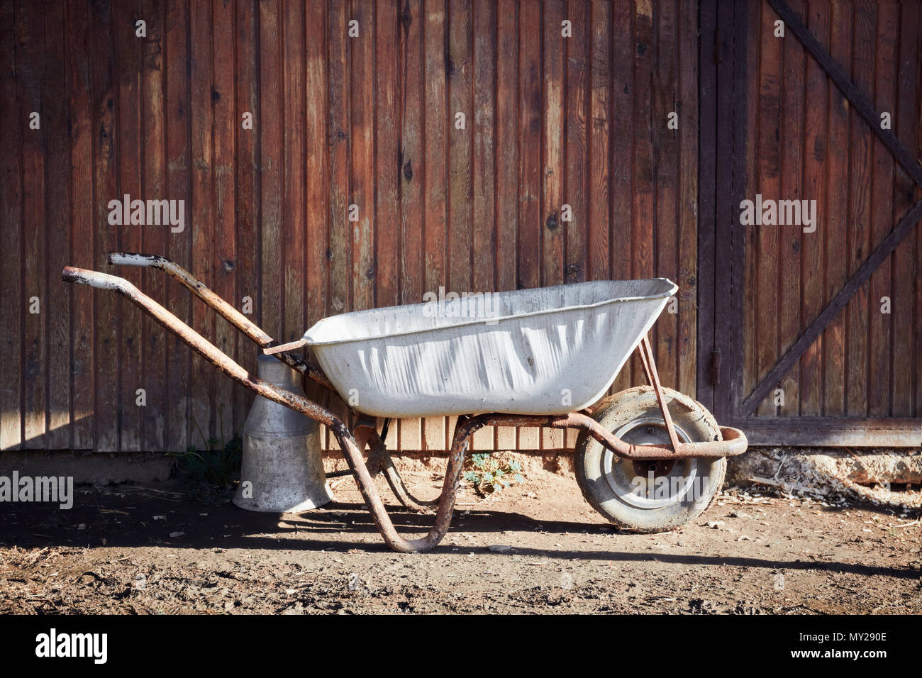 Vecchio bianco carriola vuota nella parte anteriore del legno di porta del granaio di una fattoria in una giornata di sole Foto Stock