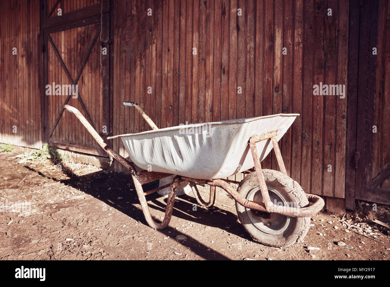 Vecchio bianco carriola vuota nella parte anteriore del legno di porta del granaio di una fattoria in una giornata di sole Foto Stock