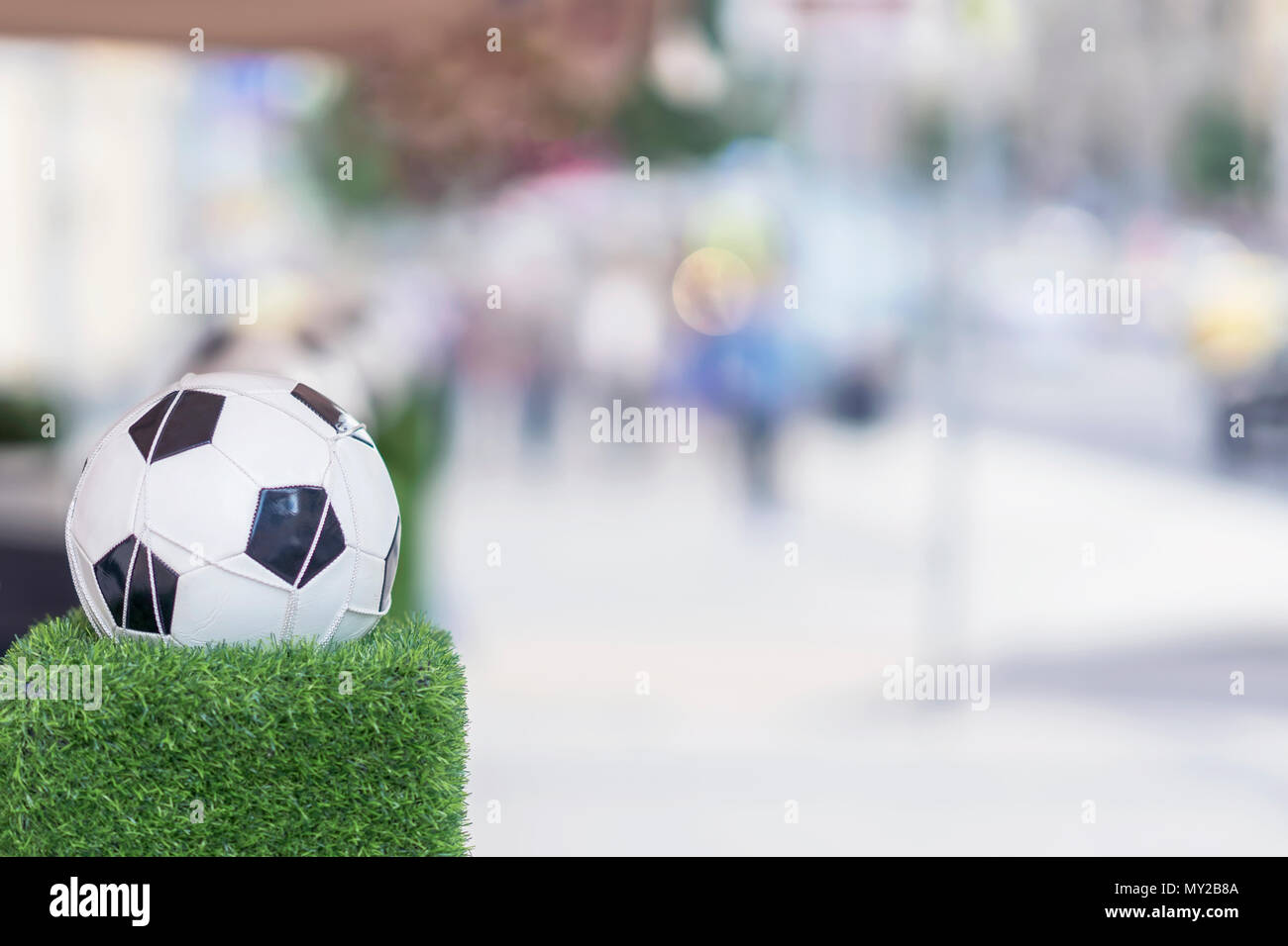 Ornamenti di strade di città in forma della classica sfera di calcio nella rete sull'erba verde. Supporto decorativo . Persone sfocate. Messa a fuoco selettiva. Foto Stock