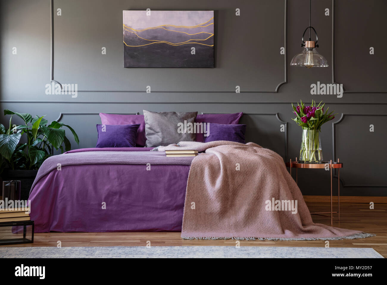 Lampada in rame sopra la tabella con i fiori accanto al letto con lenzuola viola in viola interiore camera da letto Foto Stock