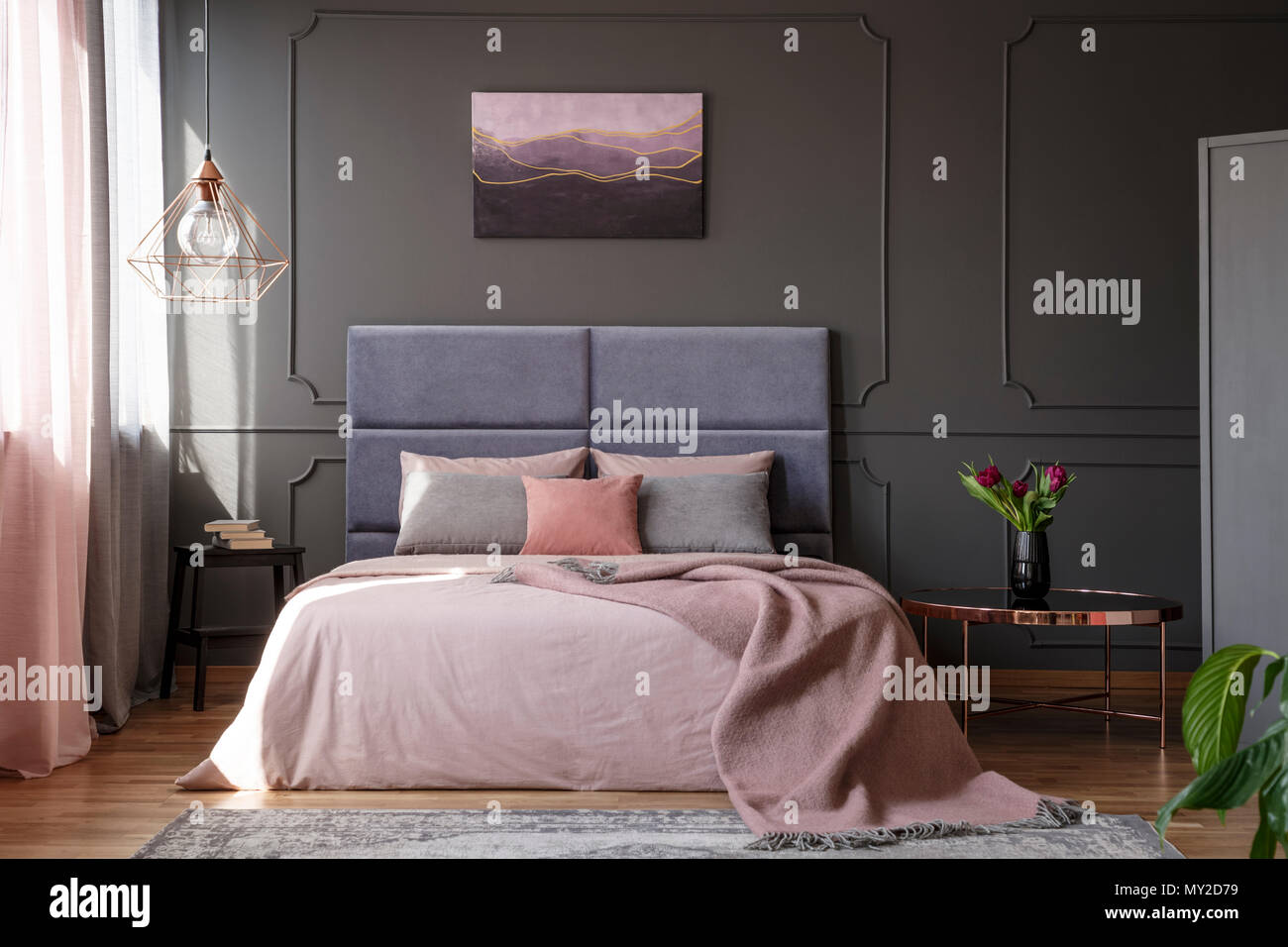 I Tulipani di rame sul tavolo accanto al letto di rosa contro la parete grigia con lo stampaggio con poster in camera da letto interno Foto Stock
