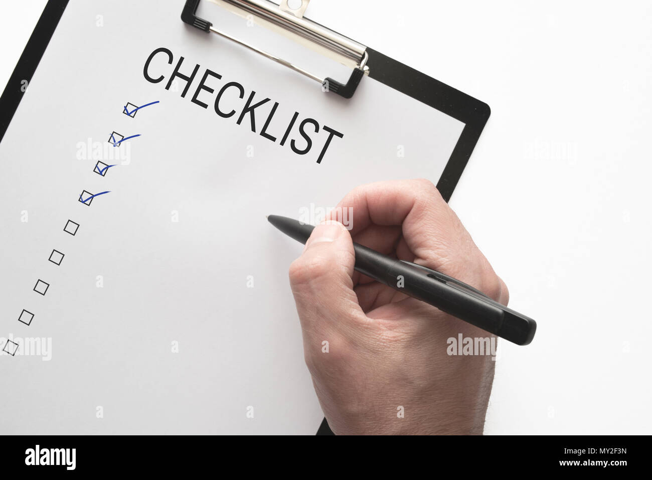 Vista superiore della mano con la penna sul clipboard con lista di controllo su sfondo bianco Foto Stock