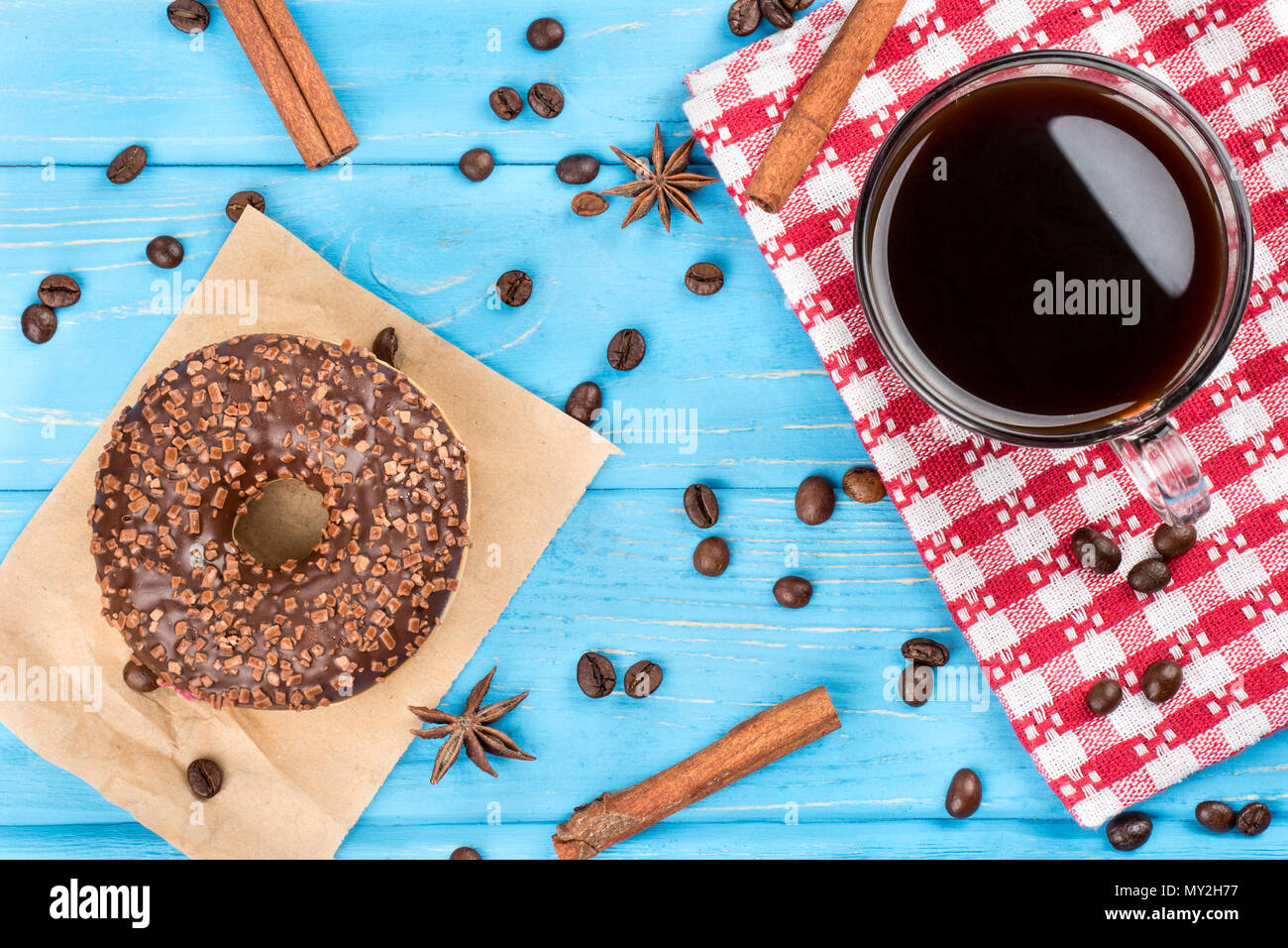 Tazza di caffè nero con una ciambella di cioccolato e granuli disseminati su un sfondo di legno, vista dall'alto Foto Stock