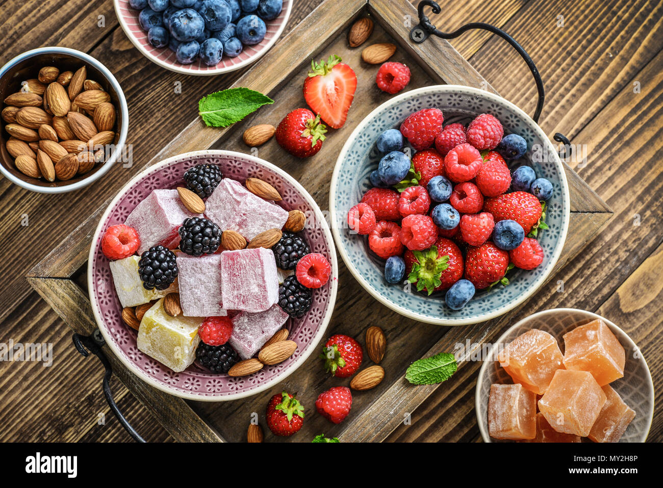 Turkish Delight con dadi e bacche di coppe in ceramica su sfondo di legno, vista dall'alto Foto Stock