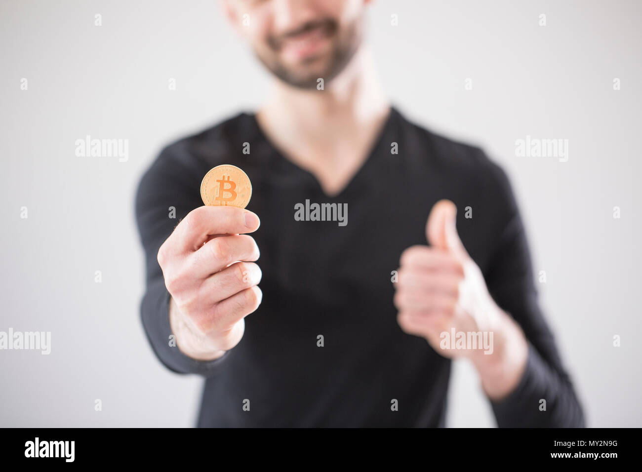 Uomo sfocata in una T-shirt nera tenendo un bitcoin e un pollice in alto Foto Stock