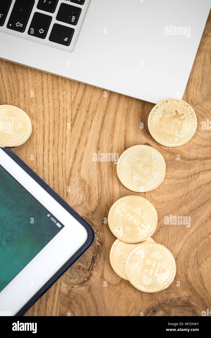 Bitcoins su un tavolo di legno accanto a un tablet e il computer portatile Foto Stock
