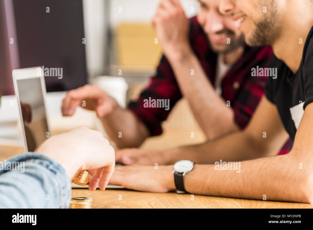 Gruppo di happy amici seduti insieme davanti a un computer portatile. Concentrarsi sulle mani dell'uomo cryptocurrency holding. Foto Stock