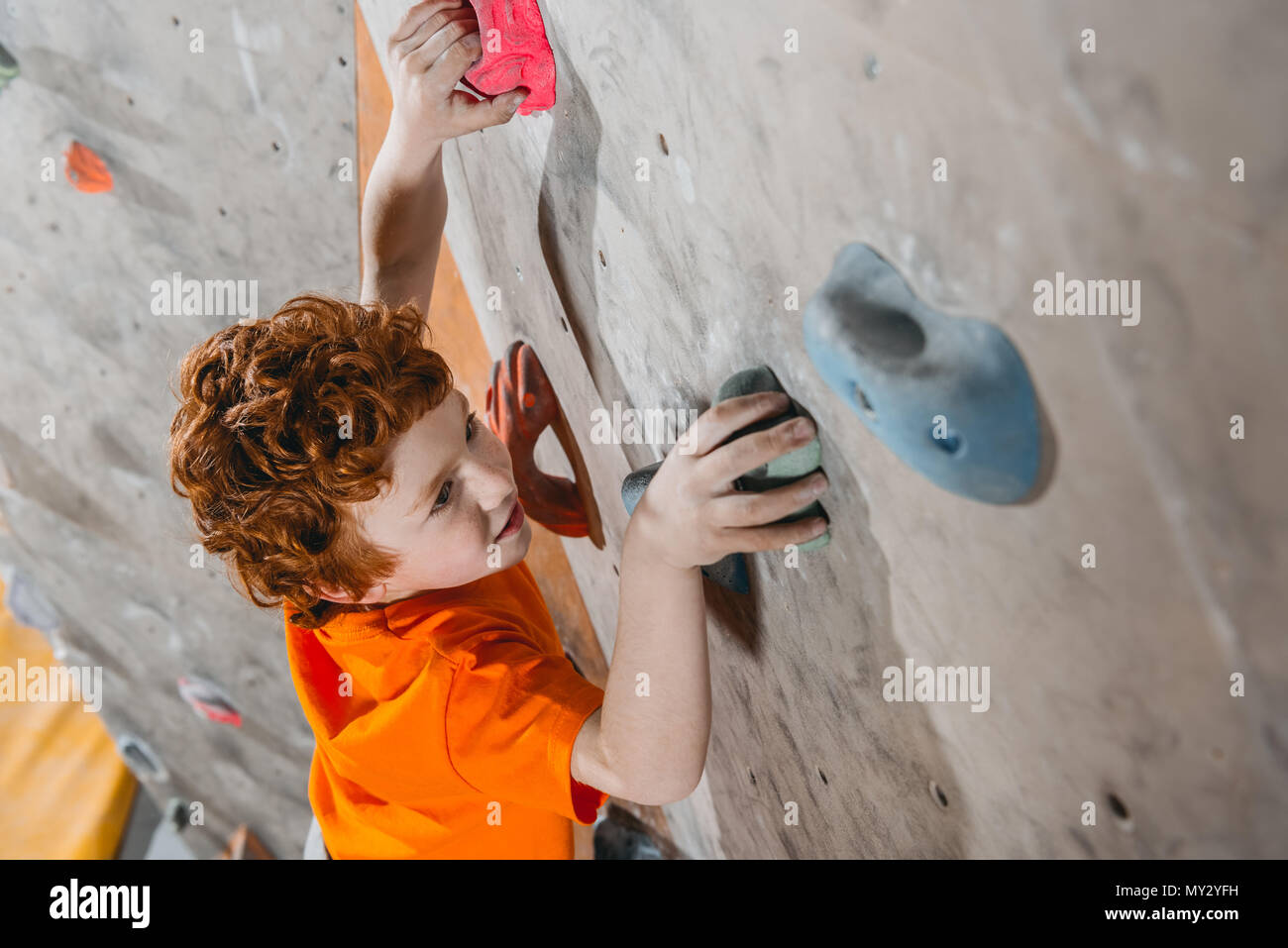 Alta angolazione di little red-headed boy salendo una parete con appigli Foto Stock