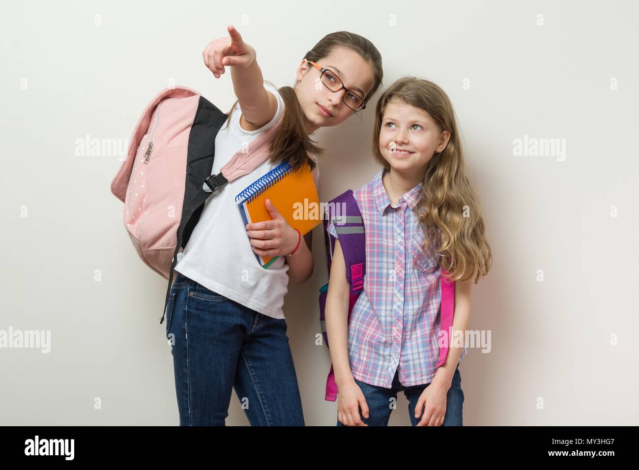 Due scolari stand con zaini sfondo parete luminosa nella scuola, cercare e visualizzare a lato. Foto Stock