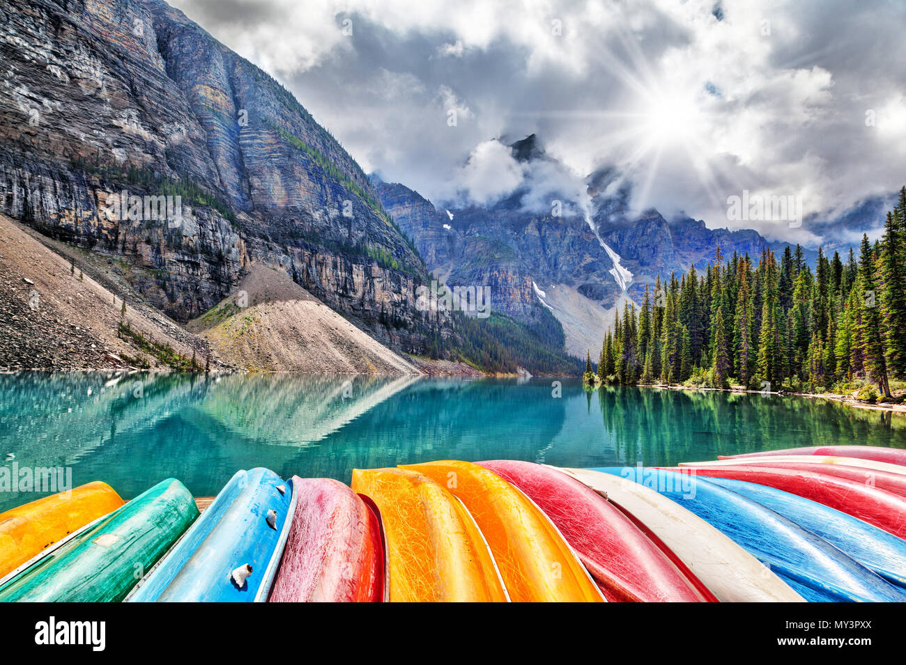 Una fila di piroghe allineate lungo le sponde del Lago Moraine al Lago Louise delle Canadian Rockies, come i picchi di sole attraverso le nuvole pesanti che è sceso sul th Foto Stock