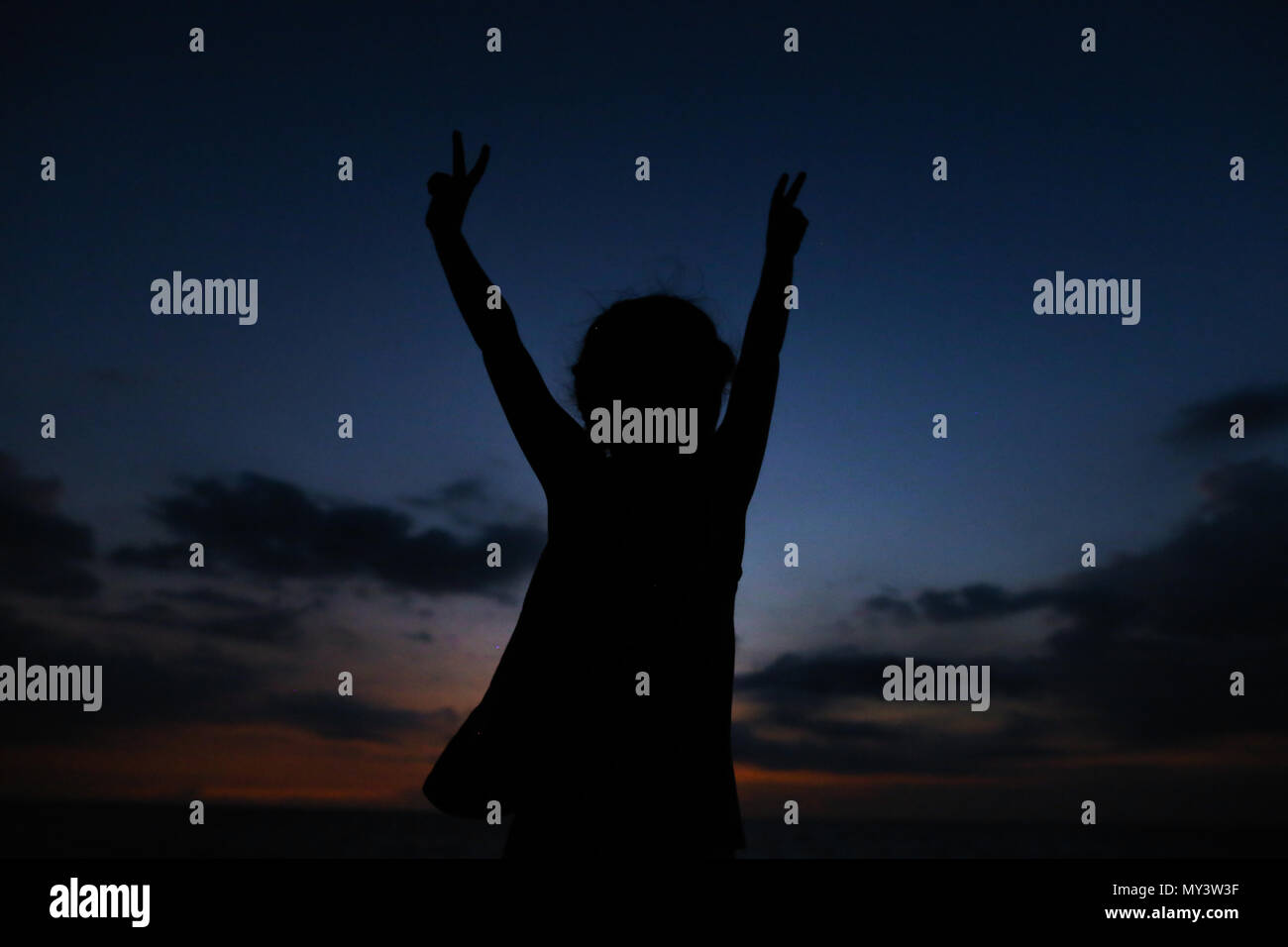 Silhouette di un piccolo bambino di sesso femminile con le mani tese nel Cielo di tramonto sullo sfondo. Foto Stock
