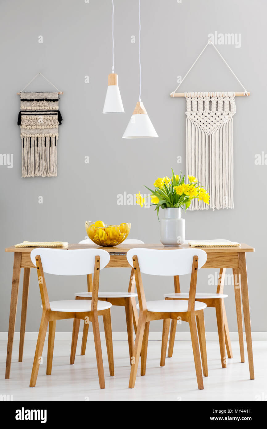 Sedie bianche al tavolo in legno con fiori di colore giallo in grigio sala da pranzo interno con lampade. Foto reale Foto Stock