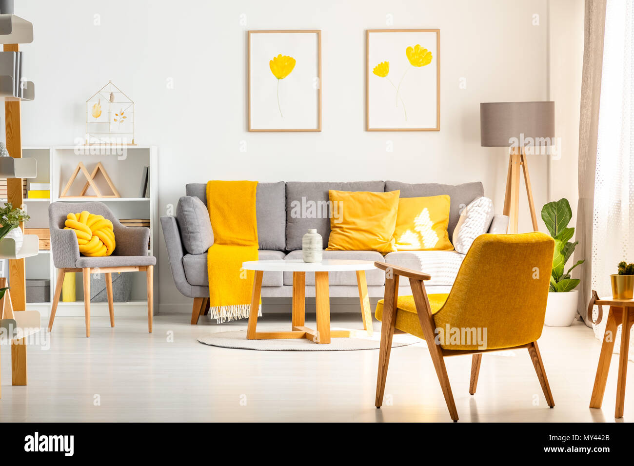 Poltrona di colore giallo in bianco salotto interno con poster sopra divano grigio con cuscini. Foto reale Foto Stock