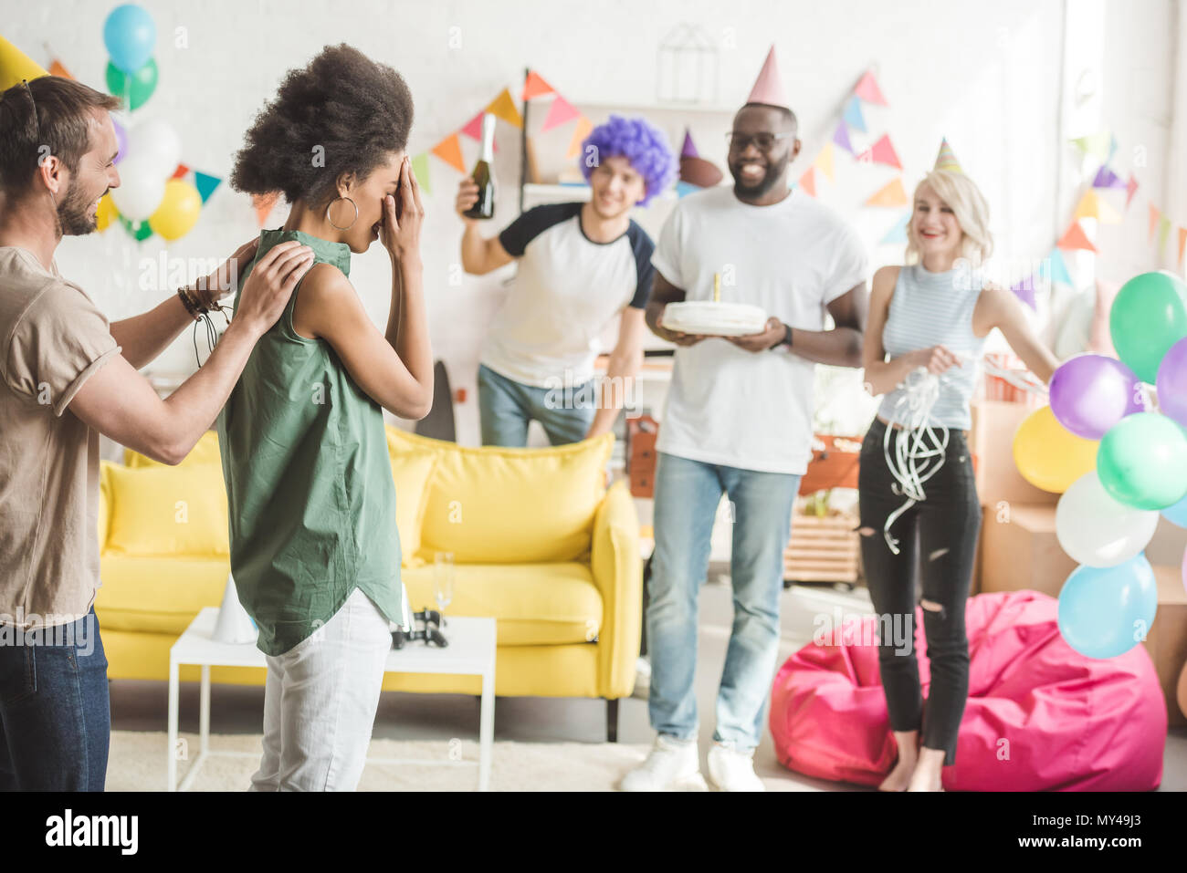 I giovani che coprono gli occhi della giovane donna e saluto lei con una torta di compleanno in festa a sorpresa Foto Stock
