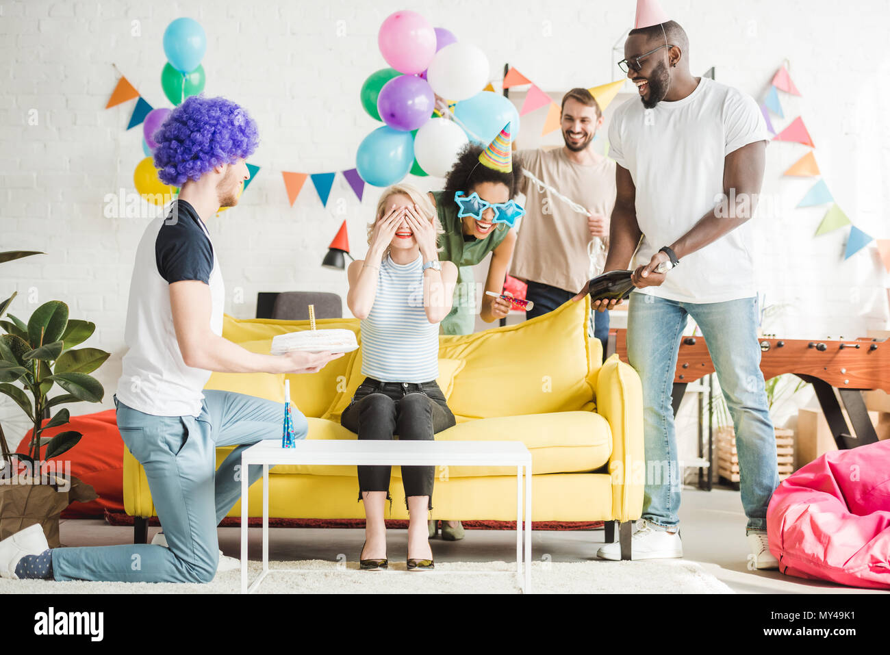 I giovani saluto donna felice con la torta di compleanno in festa a sorpresa Foto Stock