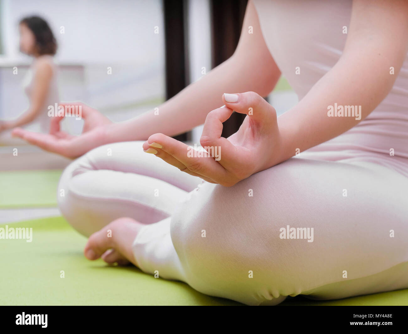 Giovane donna in tuta beige seduta sul tappeto verde e la pratica dello yoga  al light studio camera di classe. Meditando in lotus posano con Jnana Gian  mudra. Om Foto stock 