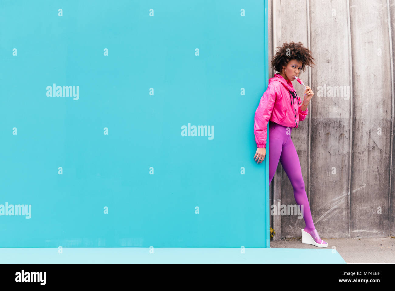 Elegante African American Girl con ghiaccioli che pongono in 80s style vestiti sul turchese Foto Stock