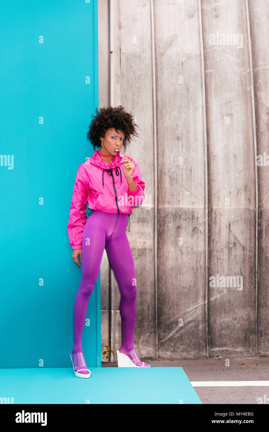 Moda ragazza afro con ghiaccioli che pongono in 80s style vestiti sul turchese Foto Stock