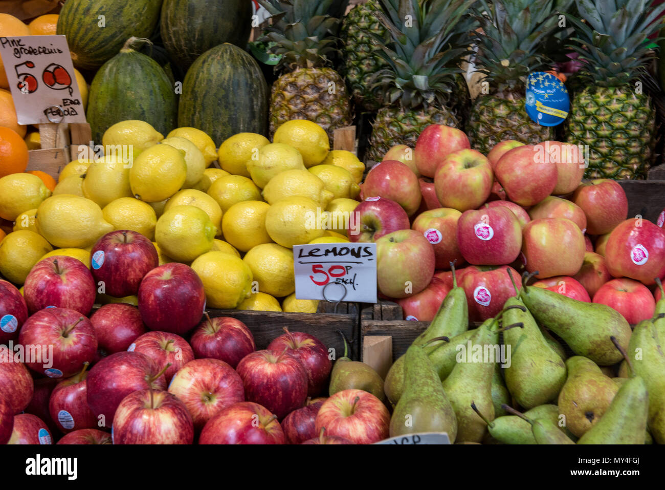 Una selezione di frutta fresca per la vendita al mercato di Borough di Londra. mele fresche, limoni, ananas e meloni su un fruttivendolo stallo trade shop store Foto Stock