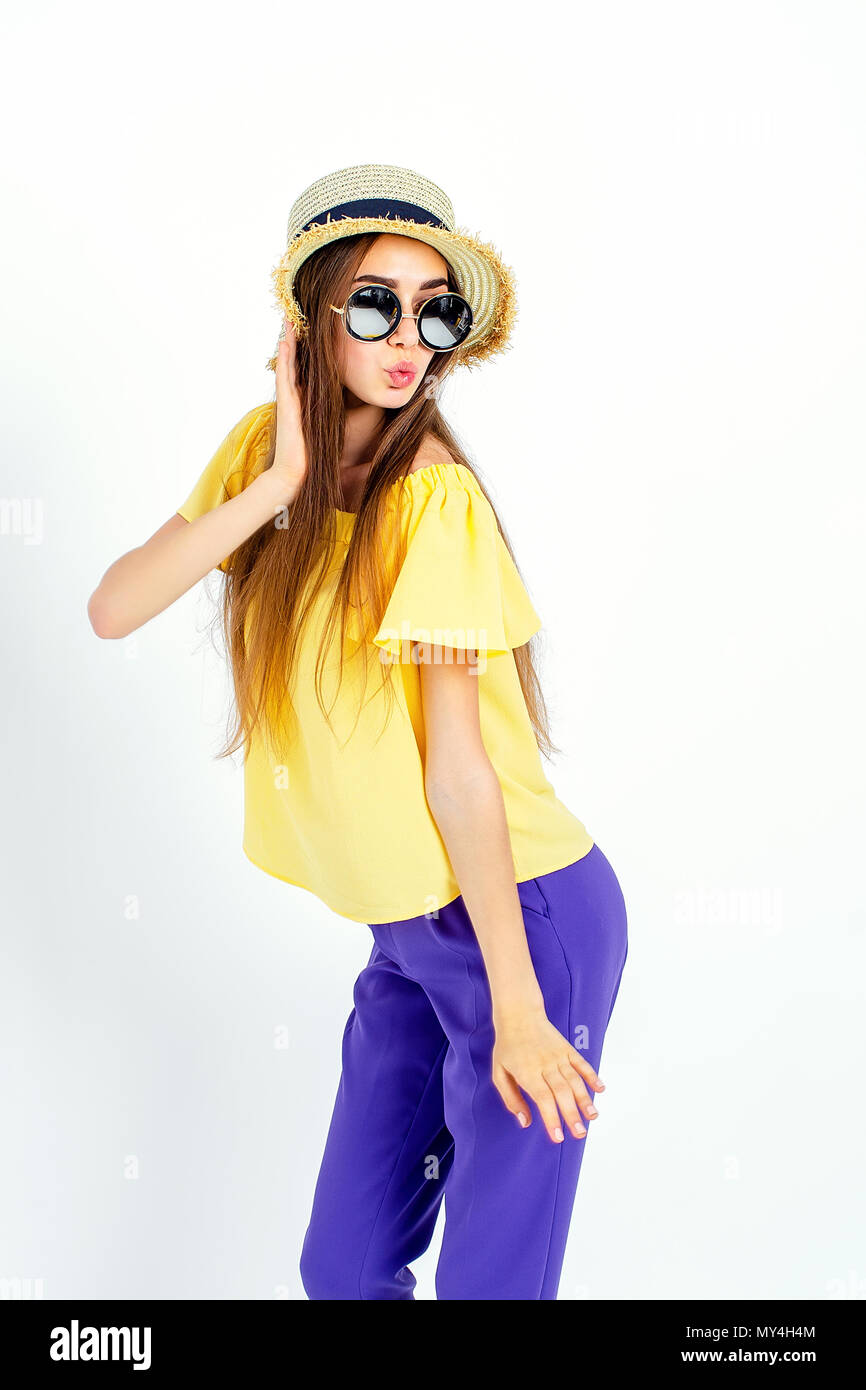 Adorabile ragazza di occhiali da sole e cappello in piedi in pantaloni color  porpora e giallo camicetta in studio su sfondo bianco Foto stock - Alamy
