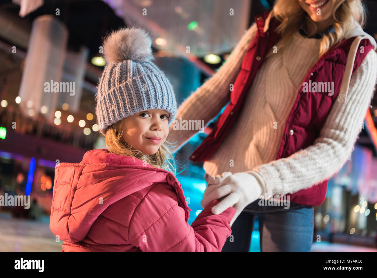 Ritagliato colpo di madre sorridente e adorabile piccola figlia tenendo le mani sul ghiaccio Foto Stock