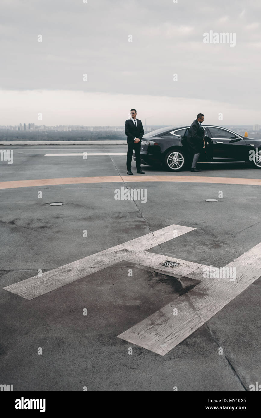 La guardia del corpo e imprenditore in piedi accanto a AUTO su elisuperficie Foto Stock