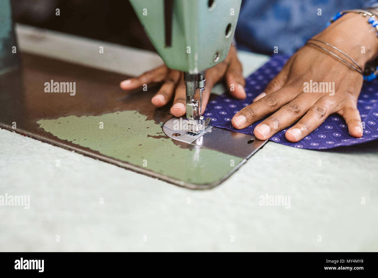 Primo piano di una sarta utilizzando una macchina di cucitura alla cucitura di un pezzo di tessuto colorato mentre si lavora nel suo negozio Foto Stock