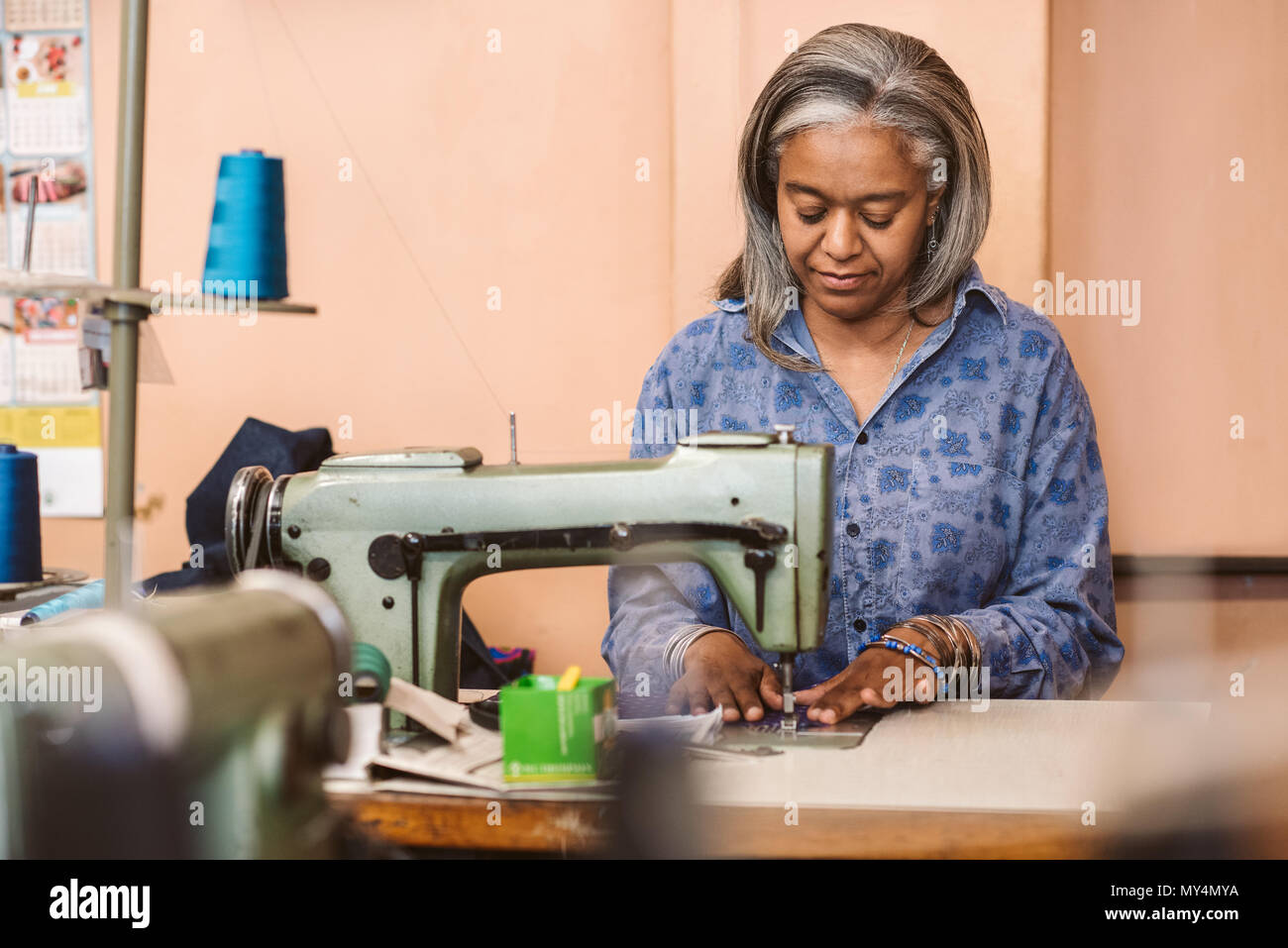 Coppia sarta seduti a un tavolo nella sua officina cucitura di un pezzo di tessuto colorato con una macchina da cucire Foto Stock