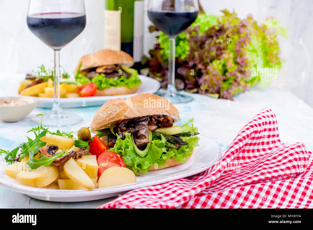 Deliziosi hamburger vegetariano e patate per tre. Insalata. Pranzo e vino. Sfondo di luce e spazio per il testo. spazio copia Foto Stock